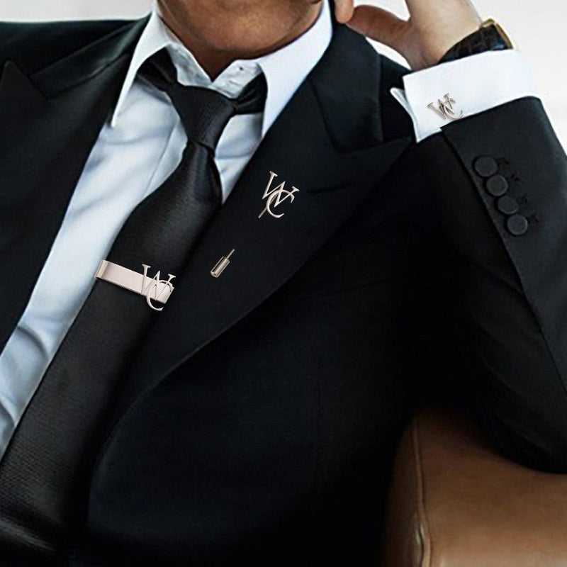 A man in a suit wearing a custom initial lapel pin, tie bar, and cufflinks set.