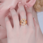 Woman wearing a gold tree of life ring with multicolored gemstones.