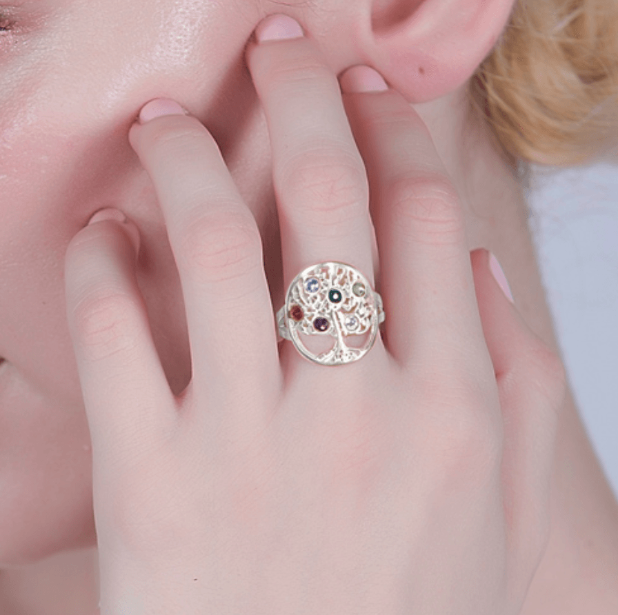 Close-up of a woman's hand wearing a gold tree of life ring with colorful gemstones.