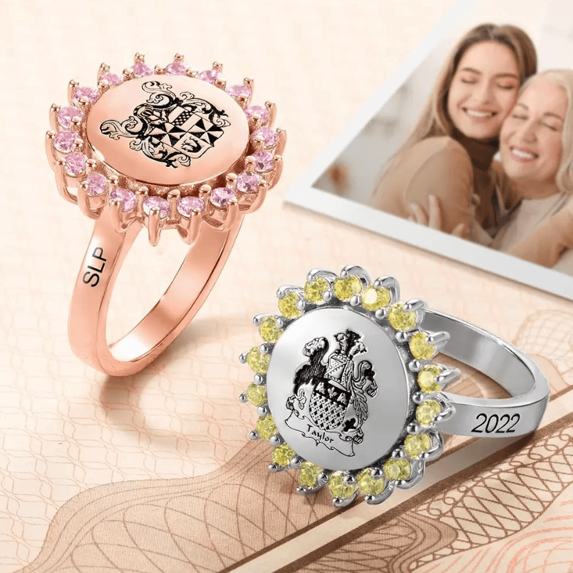 Two personalized signet rings, one in rose gold with pink gemstones and the other in silver with yellow gemstones, featuring family crests.