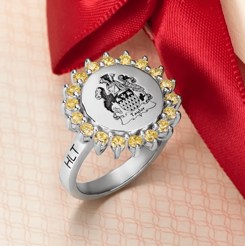 Silver signet ring with yellow gemstones around a family crest, engraved with initials 'HLT' on the band.