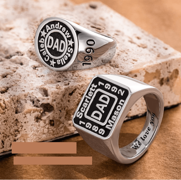 Custom engraved signet rings for men, displaying names and dates with 'DAD' in the center, set against a textured stone background.