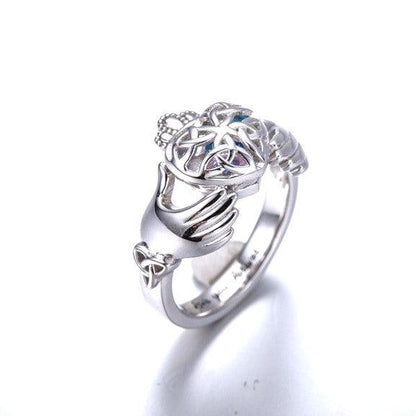 A silver Claddagh ring featuring a heart-shaped cage with a birthstone inside, flanked by two hands holding the heart, and a crown on top.