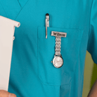 A healthcare professional in turquoise scrubs with a pen, a name badge reading "Wilson," and a silver watch clipped to the chest pocket.