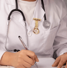 A healthcare professional in a white coat with a stethoscope, a name badge reading "Alana," and a gold watch clipped to the chest pocket, writing notes.