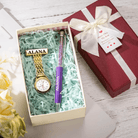 A gift box containing a gold watch and a purple pen, both labeled "Alana," with shredded paper filling, next to a wrapped gift box with a tag and flowers.