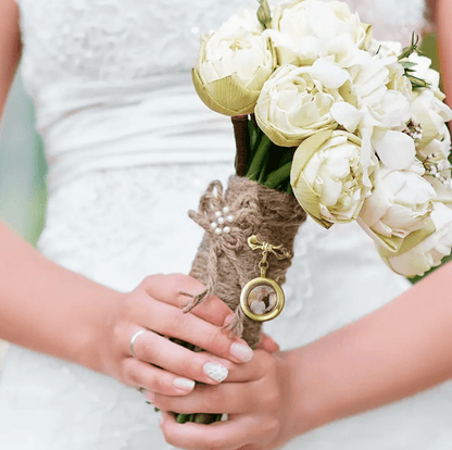A bride holding a white floral bouquet with a photo charm attached.