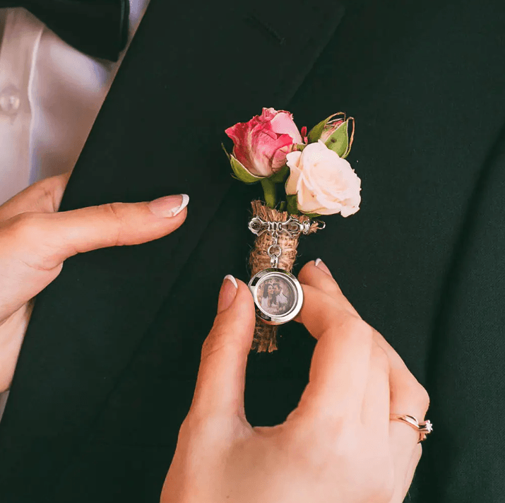 A lapel pin with a photo locket, surrounded by pink and white roses, being pinned on a suit.