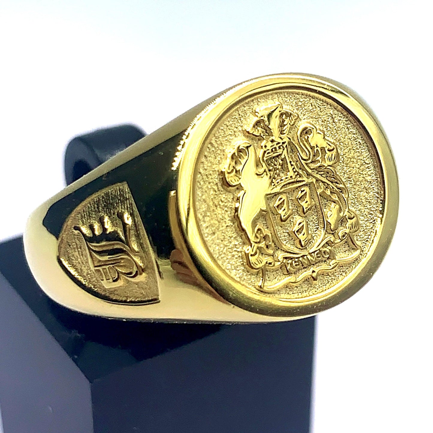 Gold signet ring featuring an embossed Kennedy family crest, detailed with a knight's helmet and shield.