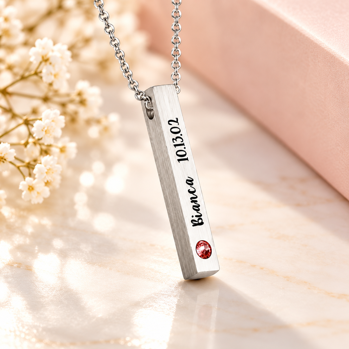 Personalized sterling silver 4-sided bar necklace with brushed finish, custom Bianca name and date engraving, and red birthstone, displayed on a luxury cream background.