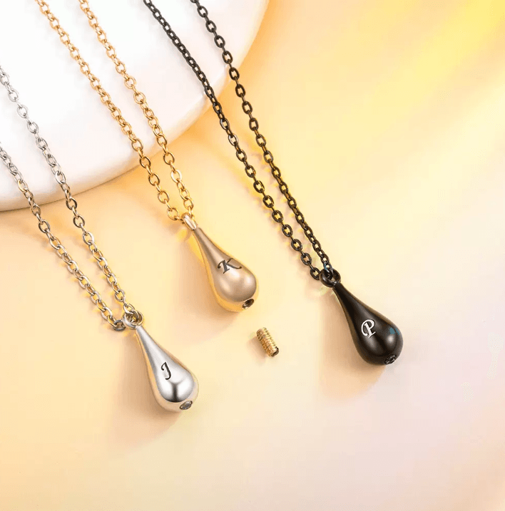 Four teardrop-shaped pendant necklaces in silver, gold, and black on a yellow surface