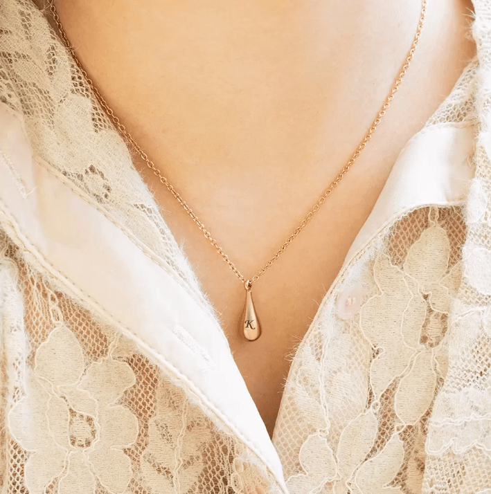 Close-up of a rose gold teardrop pendant with "K" on a lace-detailed blouse