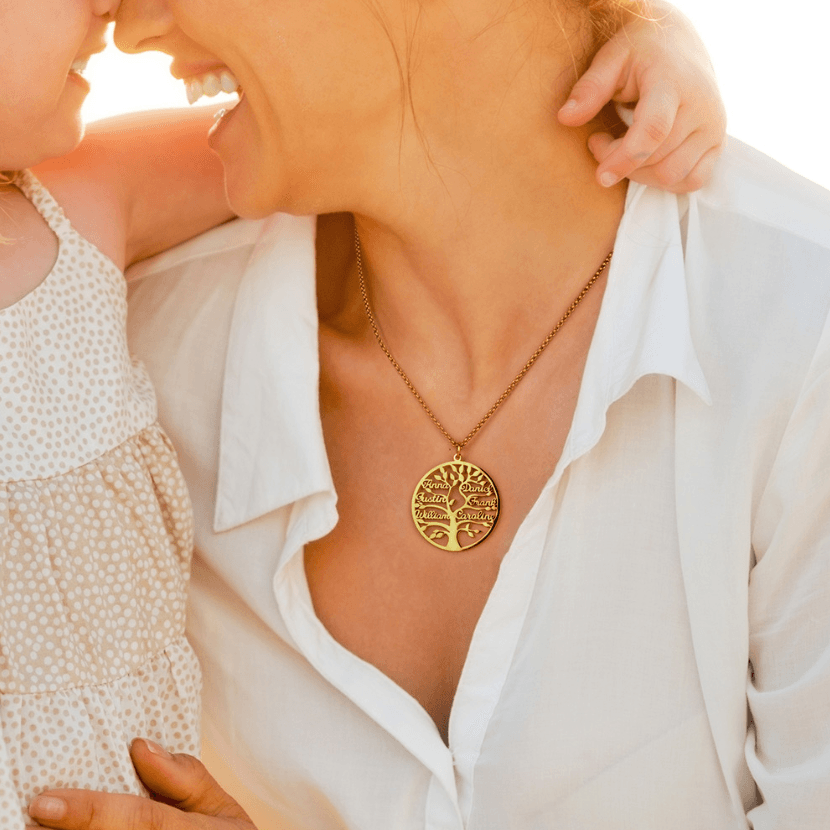 A mother wearing a gold family tree pendant necklace, smiling and touching noses with her young child, creating a warm and intimate moment.