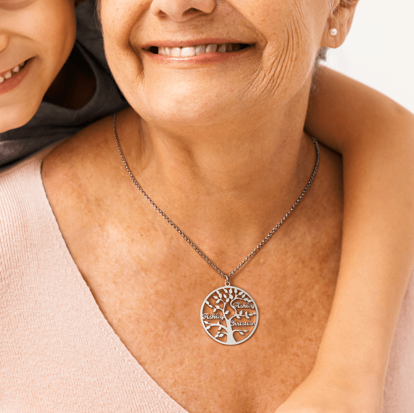 A grandmother wearing a silver family tree pendant necklace, smiling warmly as a child hugs her from behind, creating a joyful and affectionate moment.