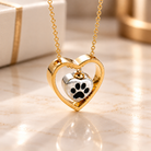 Gold heart pet memorial necklace with silver paw print charm, displayed on a soft ivory marble background.