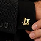 Close-up of gold entwined serif initials cufflink on a black shirt cuff with matching black suit.
