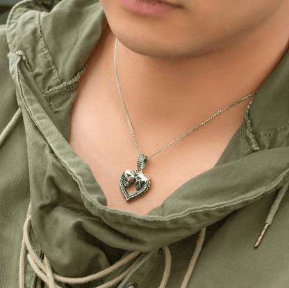 Person in green outfit wearing a silver skull heart necklace with gemstone eyes.