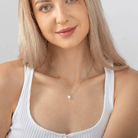 Smiling woman wearing a silver heart necklace with customizable engraving, showcasing the elegant and minimalistic design against a white top.