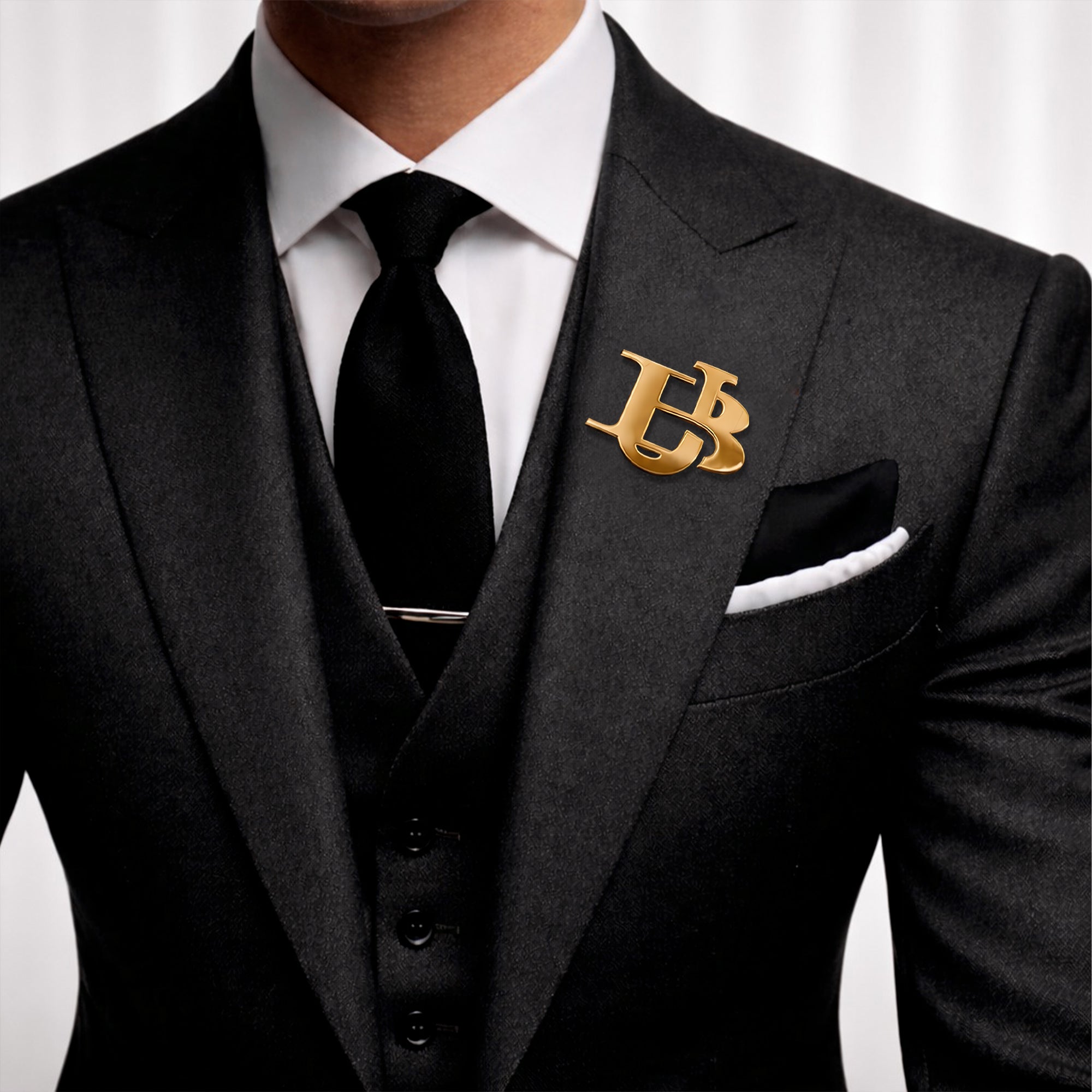Gold interlocking initials lapel pin displayed on a black formal suit