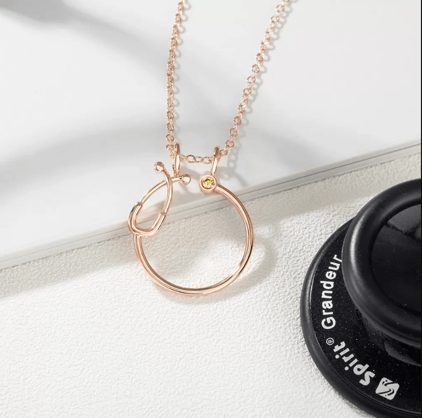 Woman wearing a rose gold ring holder necklace with a circular stethoscope design, perfect for medical professionals, featuring a customizable birthstone.