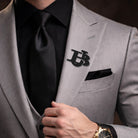 Black interlocking initials lapel pin worn on a light grey suit