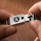 Close-up of hands clasping a Tibetan spinner bracelet clasp featuring the Om Mani Padme Hum mantra emblem