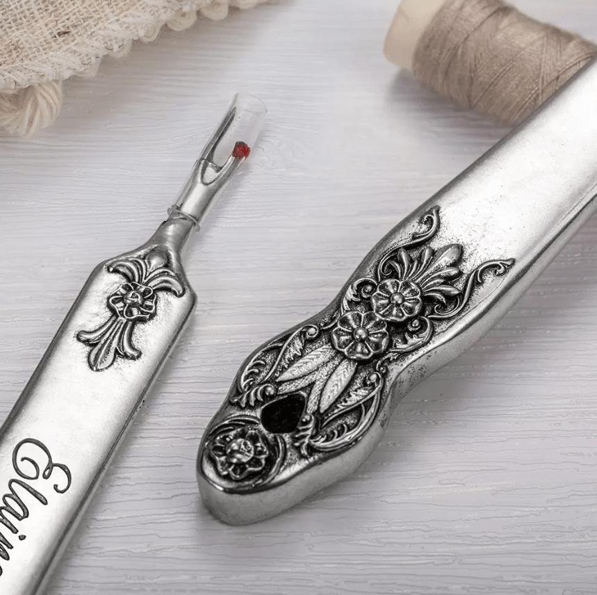 Two ornate seam rippers with floral designs, one engraved with 'Elaine' on a white background with beige thread spool