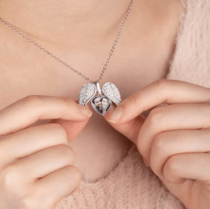 Person opening a silver angel wing locket necklace revealing a custom couple's photo.