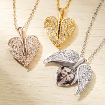 Assorted angel wing lockets in rose gold, gold, and silver with crystals, one open with a couple's photo.