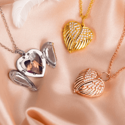 Silver and rose gold Angel Wing locket necklaces with a couple's photo displayed on satin fabric.