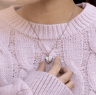 Woman in a pink sweater holding a silver angel wing heart necklace.