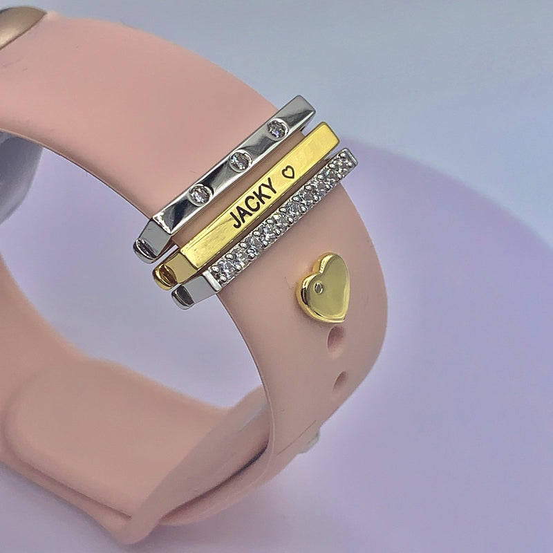 Pink Apple Watch band with personalized gold, silver, and diamond-like engraved charms featuring the name "Jacky" and a gold heart accent.