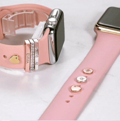 Pink Apple Watch band with personalized gold, silver, and diamond-like engraved charms featuring the name "Emma" and gold heart accents.