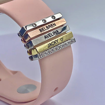Pink Apple Watch band with personalized gold, silver, and diamond-like engraved charms featuring the names "Belbren," "Avelina," and "Jacky."