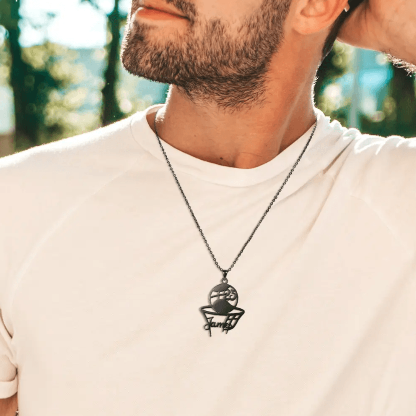 Man wearing a white t-shirt with a black basketball pendant necklace engraved with the name 'James' and number '23'.