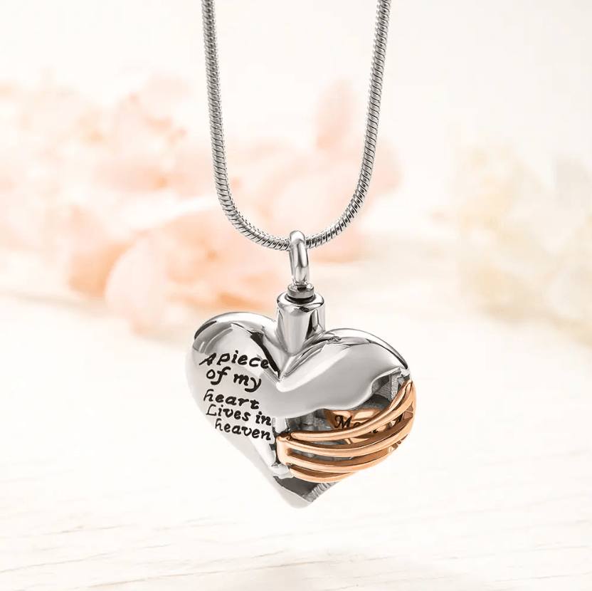 Heart-shaped pendant with the inscription "A piece of my heart lives in heaven," featuring a gold ribbon with the word "Mom," on a silver chain.