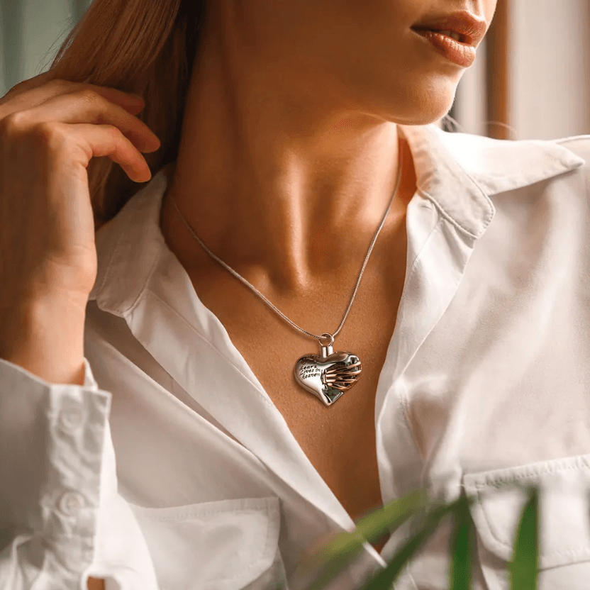 Woman wearing a heart-shaped pendant with the inscription "A piece of my heart lives in heaven" and a gold ribbon design, on a silver chain.