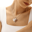 Woman wearing a heart-shaped pendant inscribed with "A piece of my heart lives in heaven," featuring a gold ribbon design, on a silver chain.