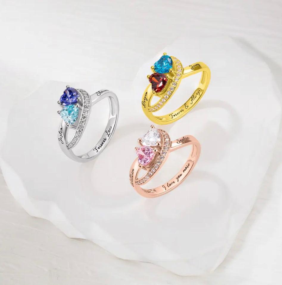 Three rings with heart gems and engravings; one silver, one gold, one rose gold, on a white surface.