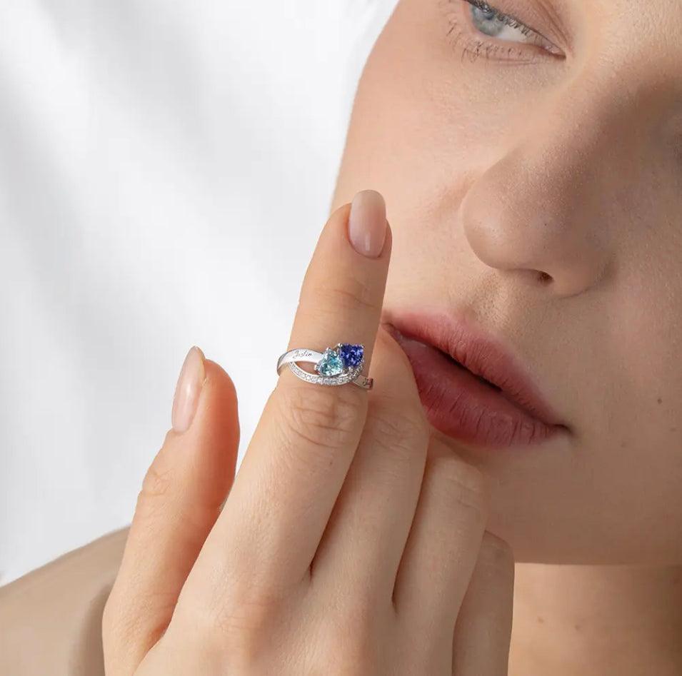 A person wearing a silver ring with a blue gem on their finger, partial face visible in the background.