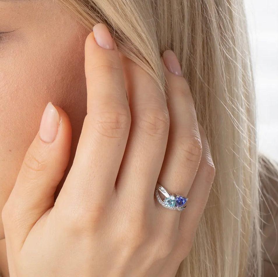 A close-up of a hand with a silver ring featuring a blue gem, against a woman's blonde hair.