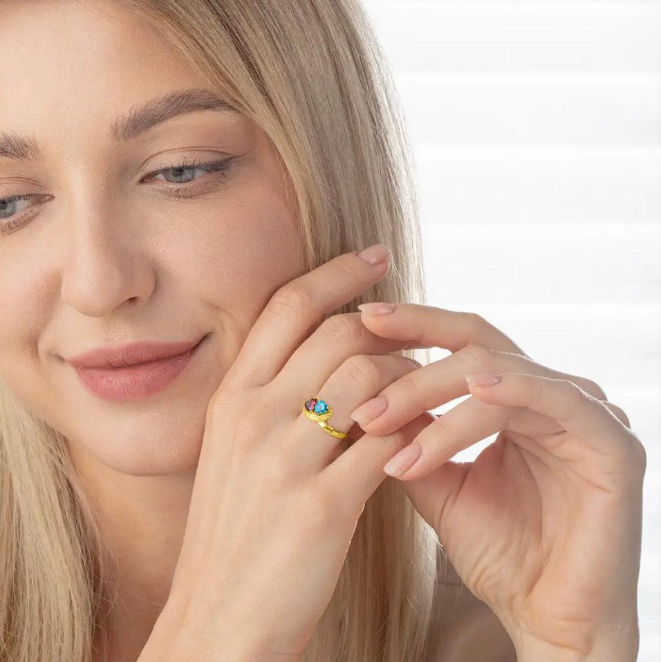 Smiling woman with a gold ring and blue gemstone on her finger, touching her face.