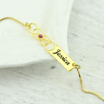 Personalized Double Infinity Knot Necklace with Birthstone in Gold, featuring the name "Jessica" engraved on a rectangular pendant, displayed on a white surface.