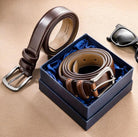 Elegant brown leather belt with a classic silver buckle, presented in a navy blue gift box with sunglasses to the side.