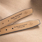 Two tan leather belts with loving messages engraved for an anniversary and a father, laid out on a textured surface.