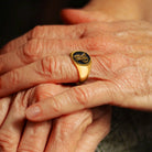 Gold tone personalized initials signet ring with black engraved face shown on a hand.
