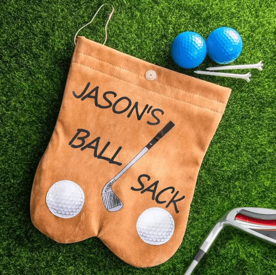 Custom tan flannelette golf ball sack labeled 'Jason's Ball Sack' on grass, with golf balls, tees, and a club nearby, showcasing a humorous and personalized design.