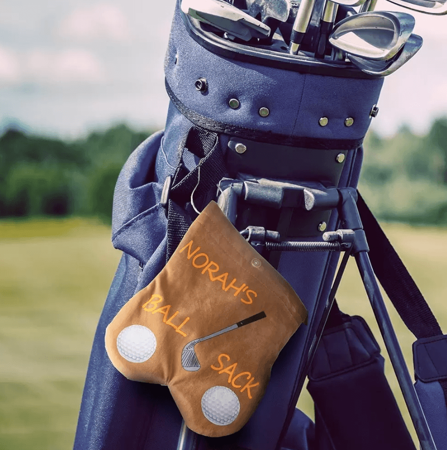 Norah's Ball Sack' attached to a navy blue golf bag, set against a serene golf course backdrop, highlighting a tailored, handy golf accessory.