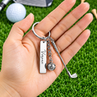 Personalized golf keychain with custom name, golf club and ball charms held in hand on green grass