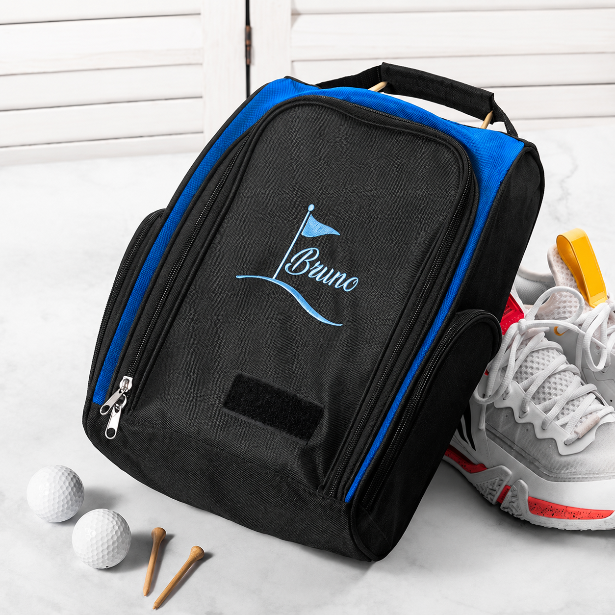 Black and blue personalized golf shoe bag displayed with golf shoe and golf accessories